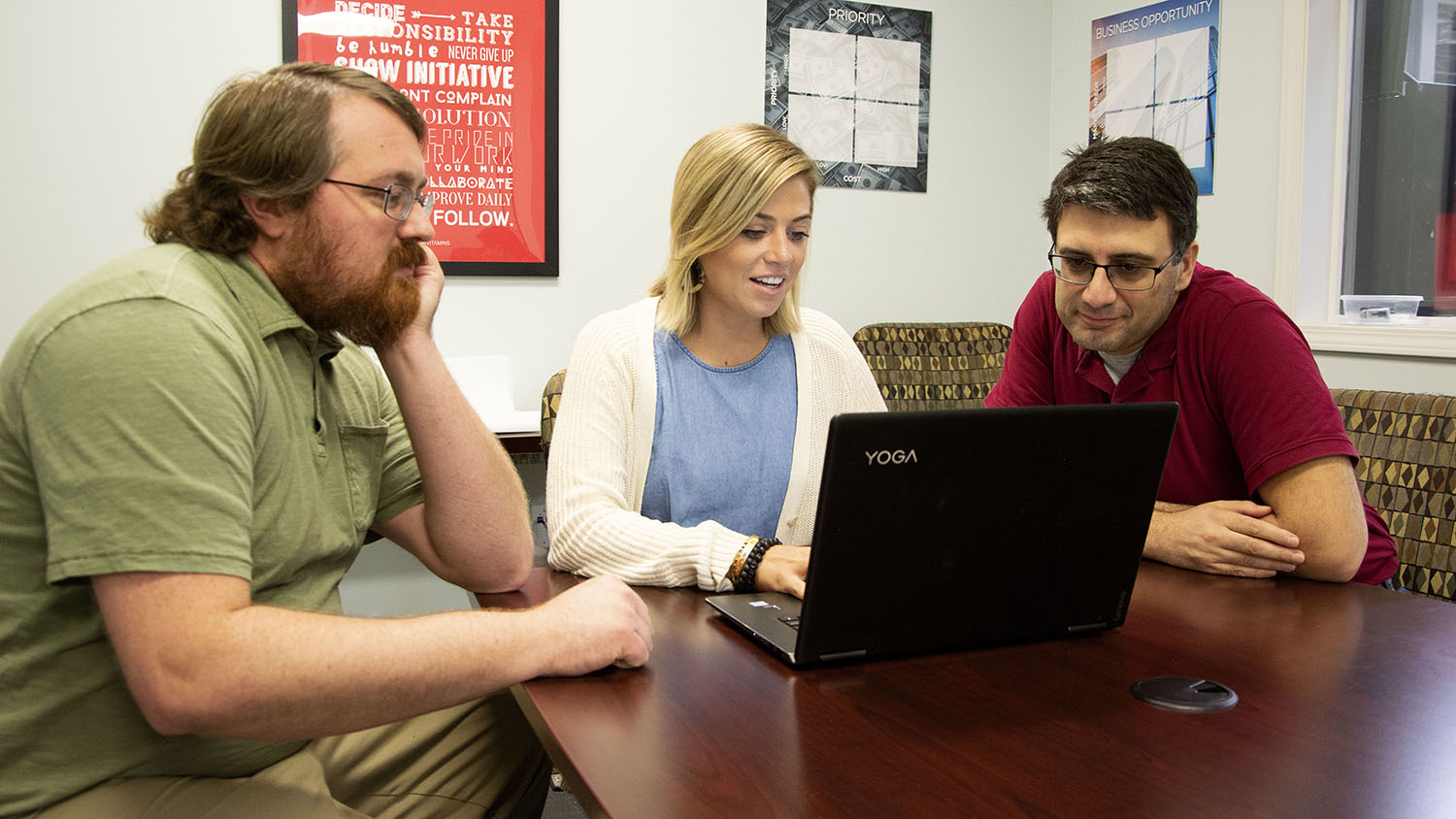 Caroline Olson, a Kenan Fellow, types on a laptop at a table as her two mentors look over her work.