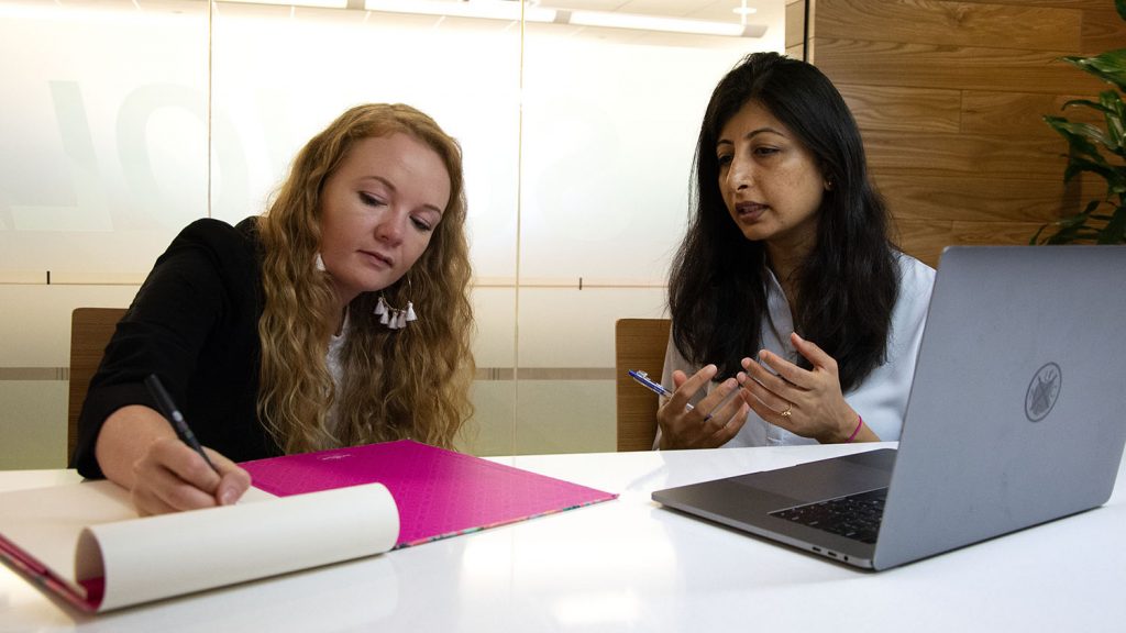 Taylor Waters, a Kenan Fellow, takes notes next to a Fidelity Investments worker in an office.