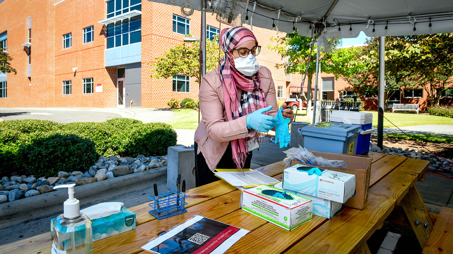 masked and gloved woman working at COVID testing tent on NC State's campus