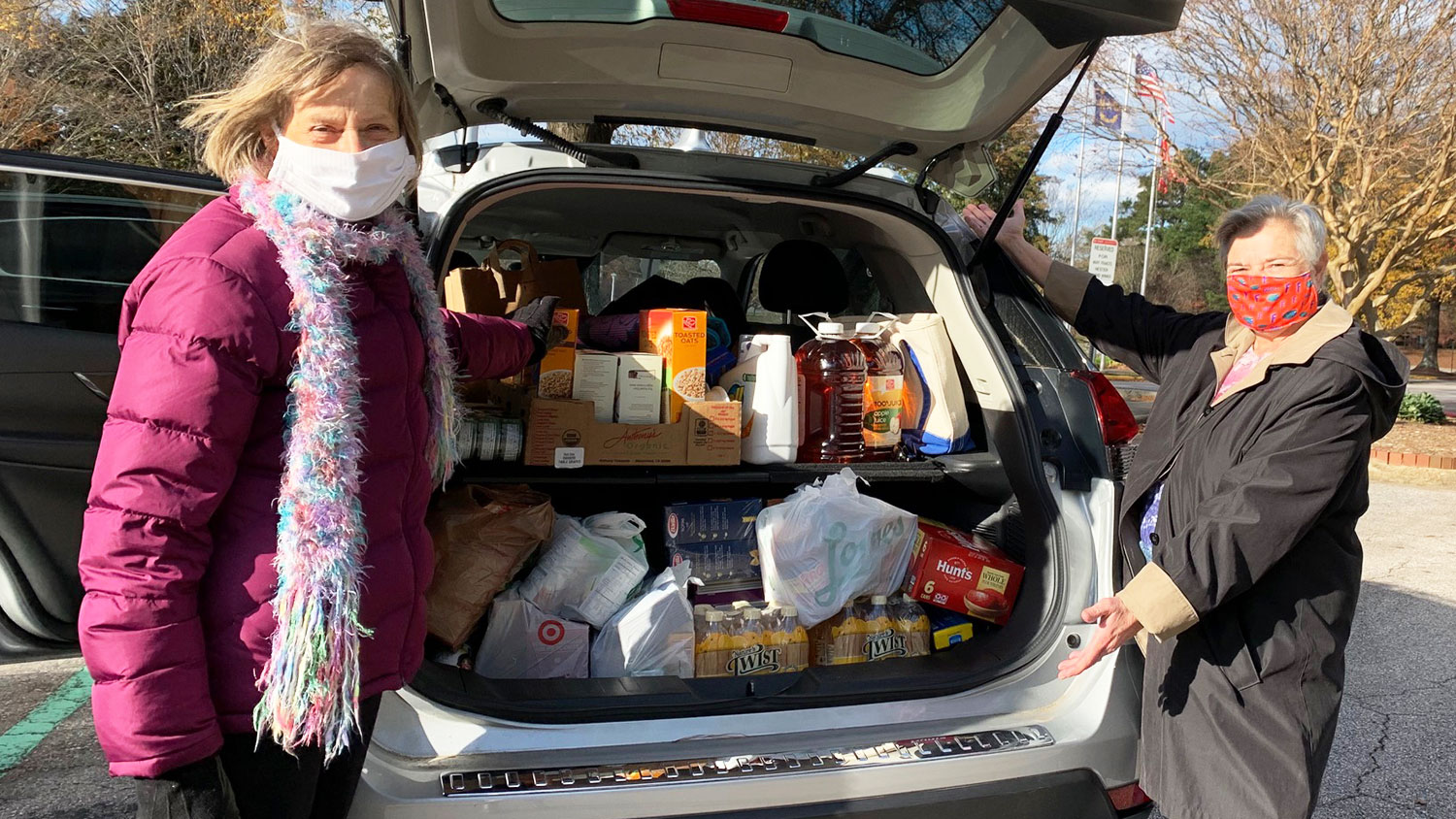 two women standing next to car packed with food donations