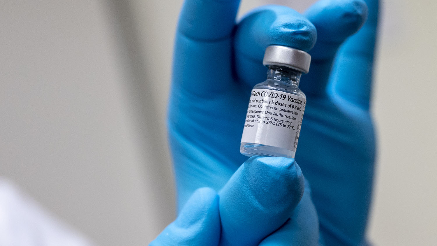 hand in latex glove holding a vial of COVID-19 vaccine