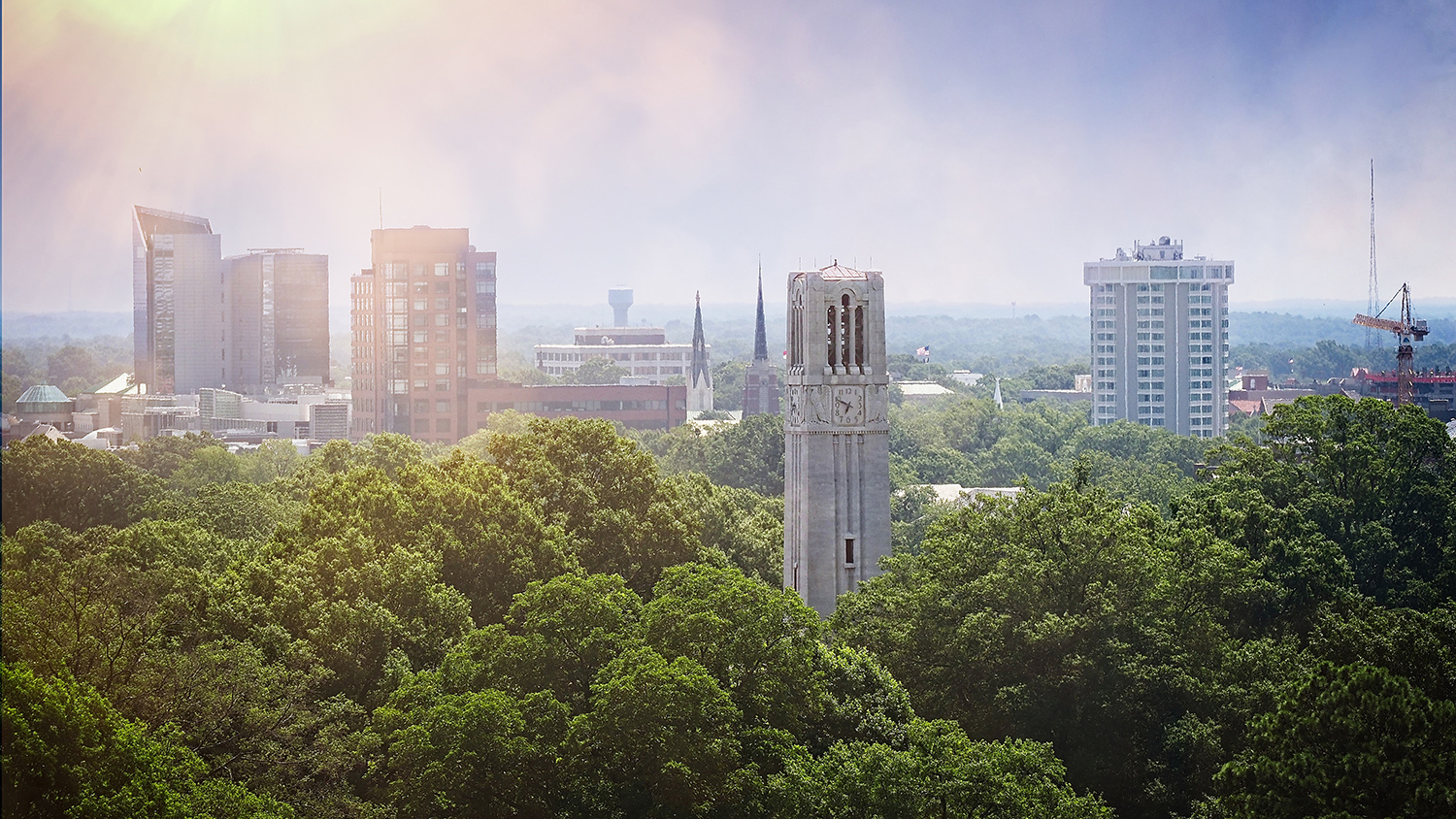 The NC State belltower sits in front of the city of Raleigh skyline as seen from a DH Hill library window.