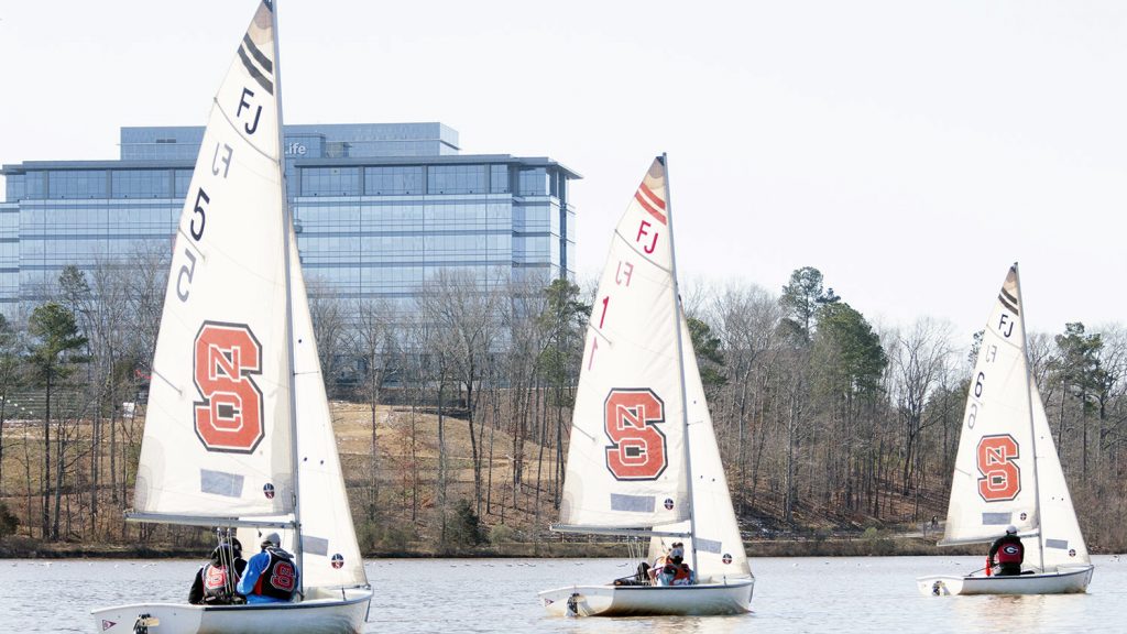 Three sailboats with the NC State block S logo on their sails on a lake