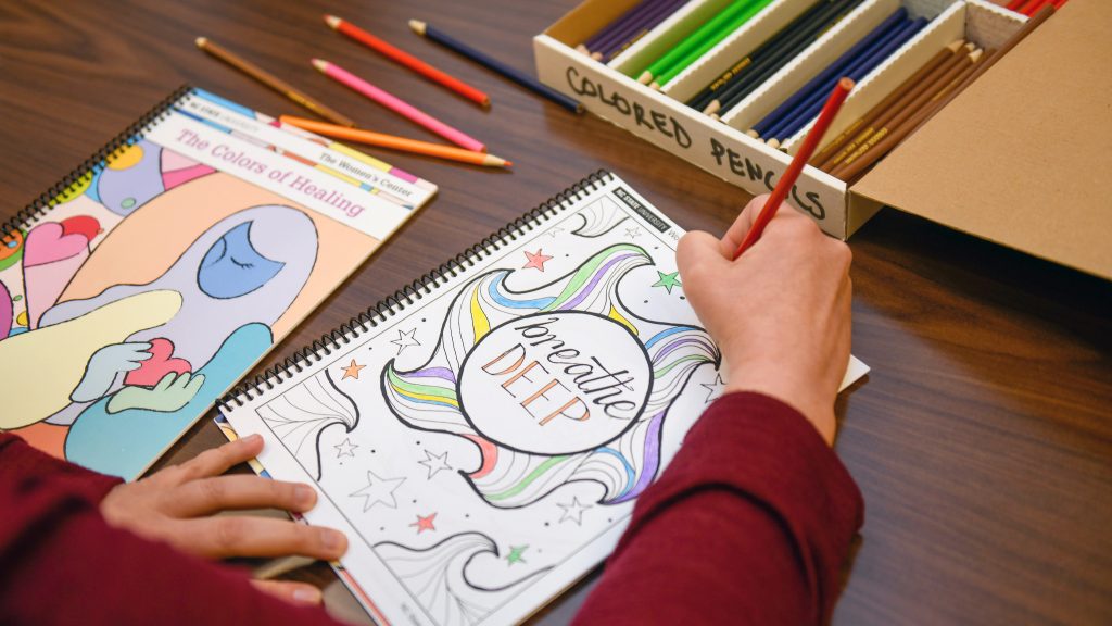 A hand colors in a coloring book page that reads "Breathe Deep."