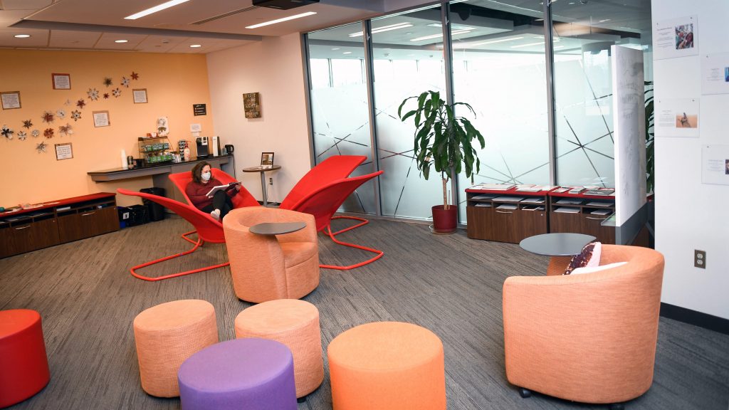 A woman wearing a face mask sits alone in the bright lobby of the NC State Women's Center.