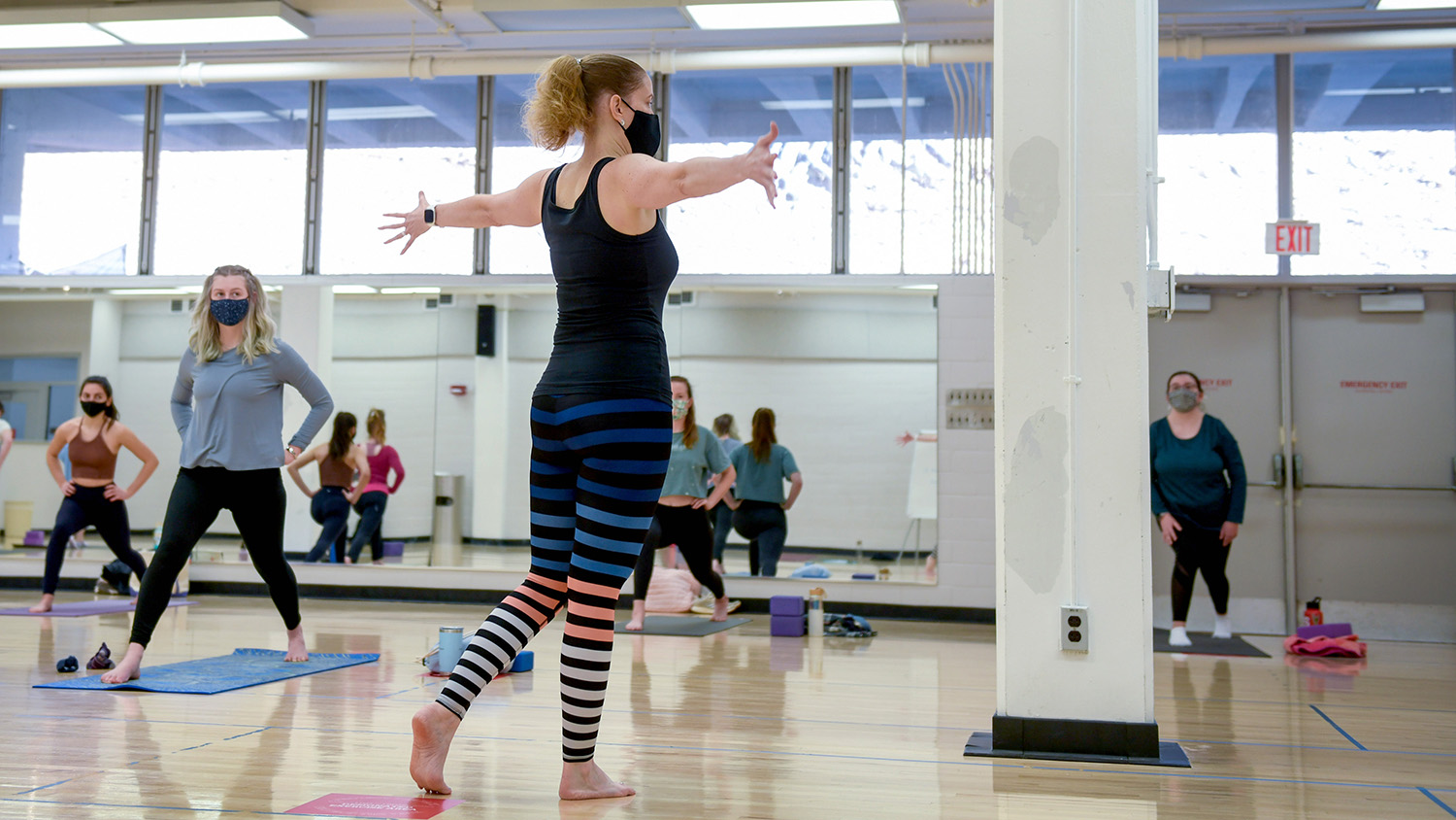 Autumn Belk stands with her arms outstretched, back to the camera, teaching students a yoga pose.