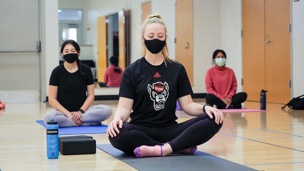 Students sit on the floor of the gym and meditate.