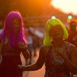 Two young women in colorful wigs dance down Hillsborough Street.