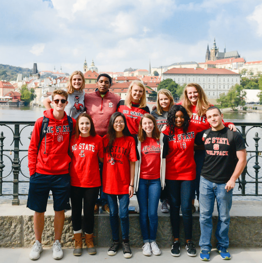 A group of students wearing red pose for a photo together on a bridge in Prague.