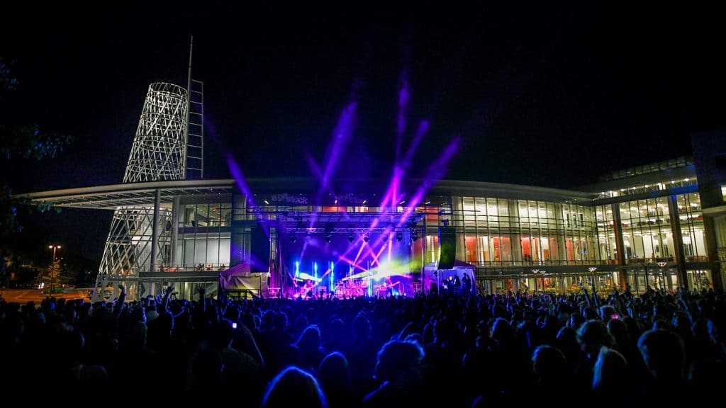 A large crowd watches a concert with brightly colored lights outside of Talley Student Union.