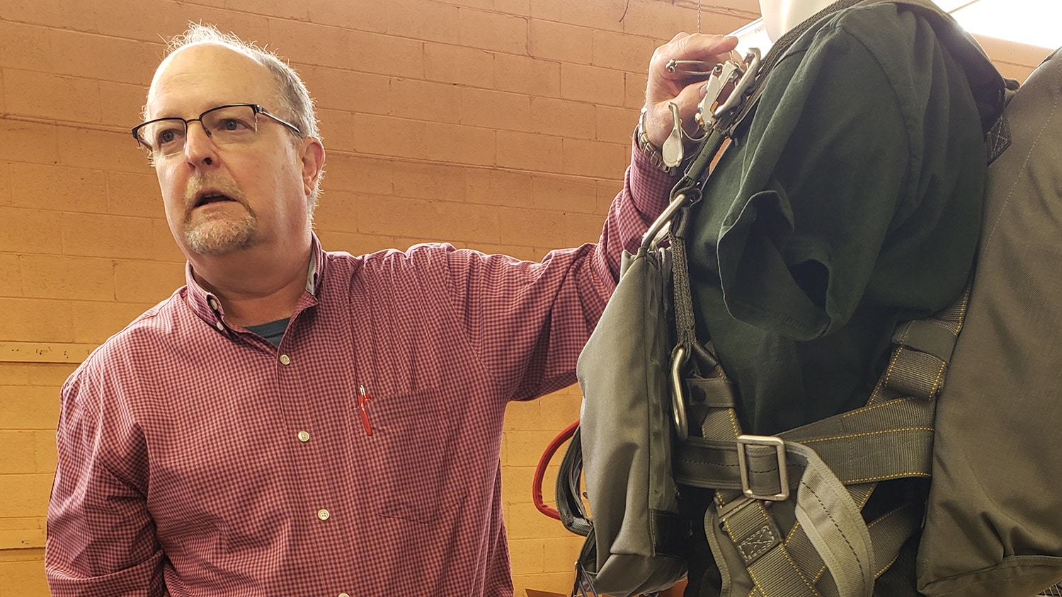 Dan Swift, a Mills Manufacturing worker, a T-11 parachute individual harness to shows IES personnel during a company tour.