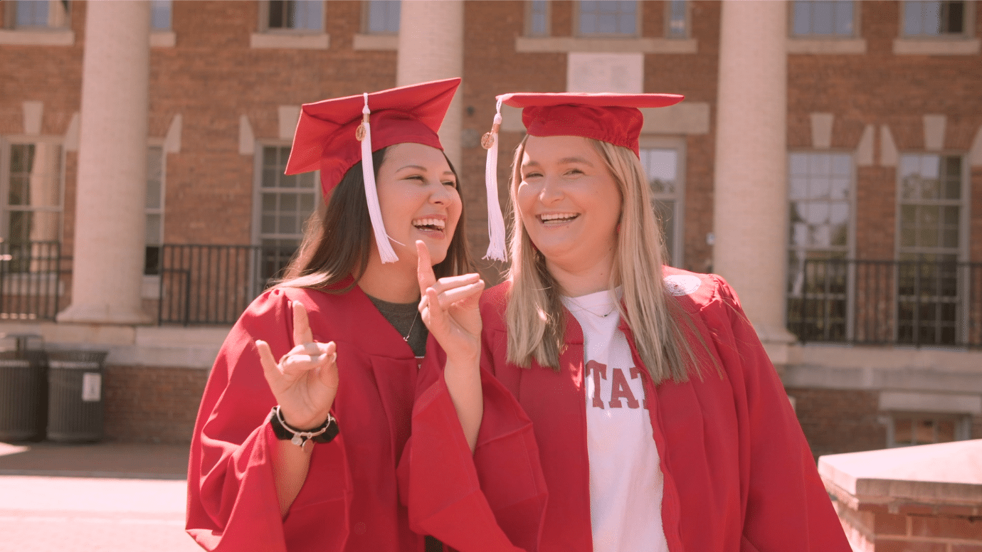 Emily Barefoot and Mary Kathryn Kinley pose in their grad caps and gowns while holding up wolf ears at the Court of North Carolina.