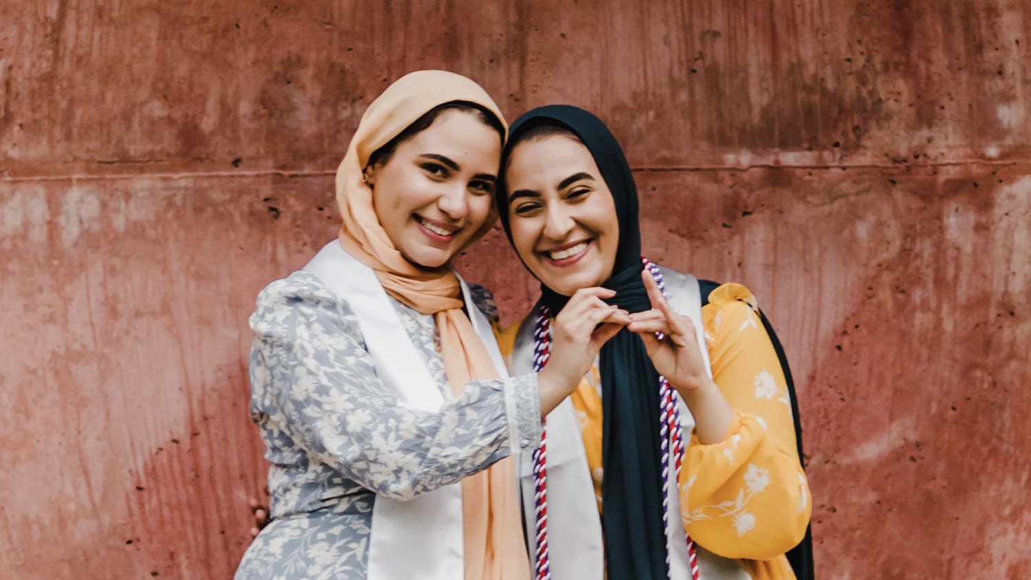 Twin sisters Iman, left, and Salam pose together at a Wolf Ears sculpture on campus and make wolf hands gestures. 