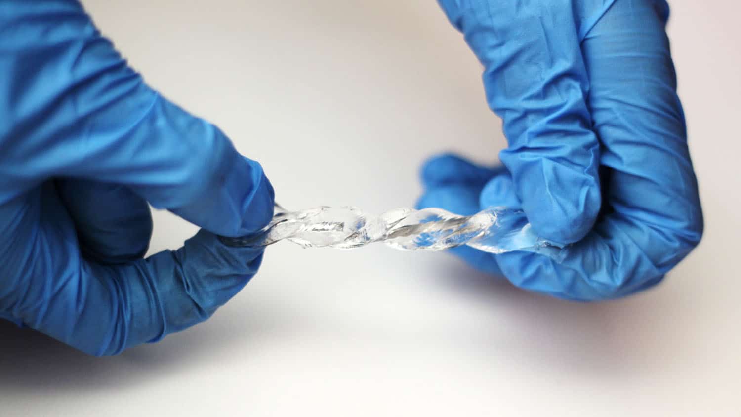 hands in latex gloves twist a piece of clear, elastic material that contains liquid metal