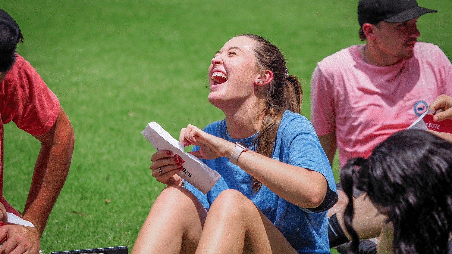 A student laughs while sitting on the field during convocation.