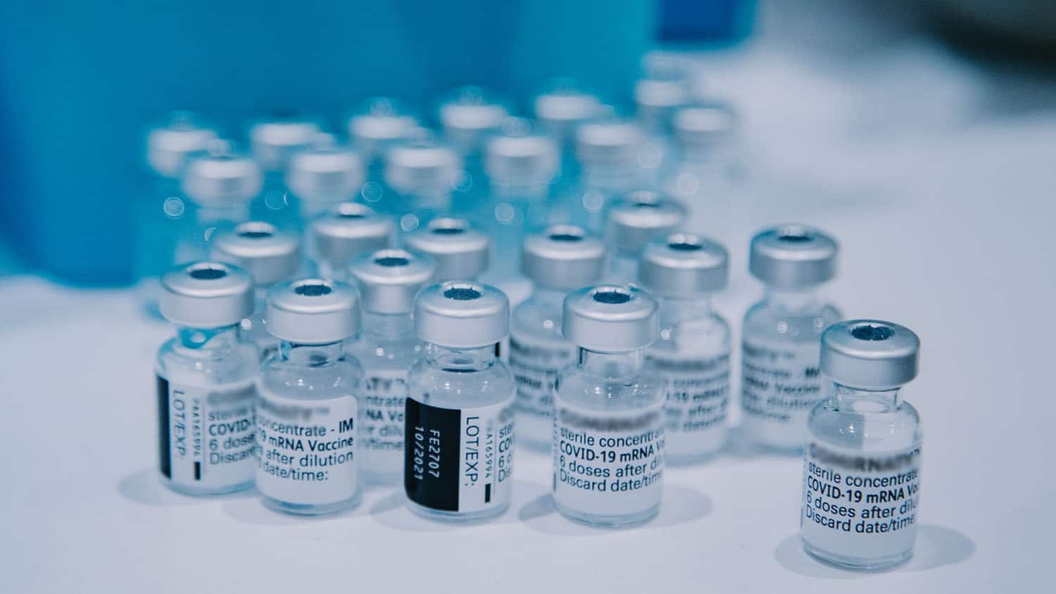 cluster of bottles containing covid-19 vaccine sit on a white counter