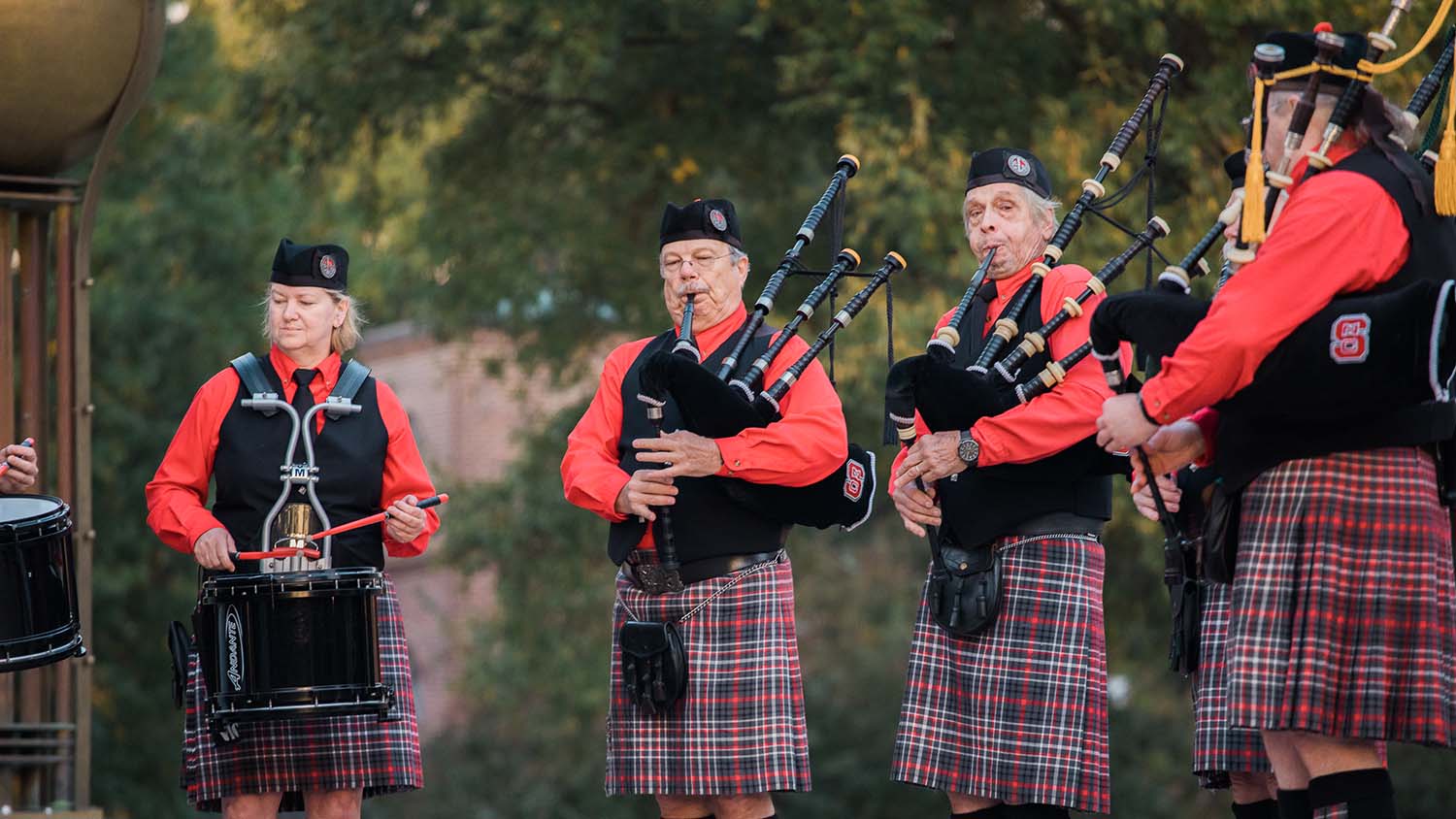 Four people wearing kilts and playing bagpipes. 