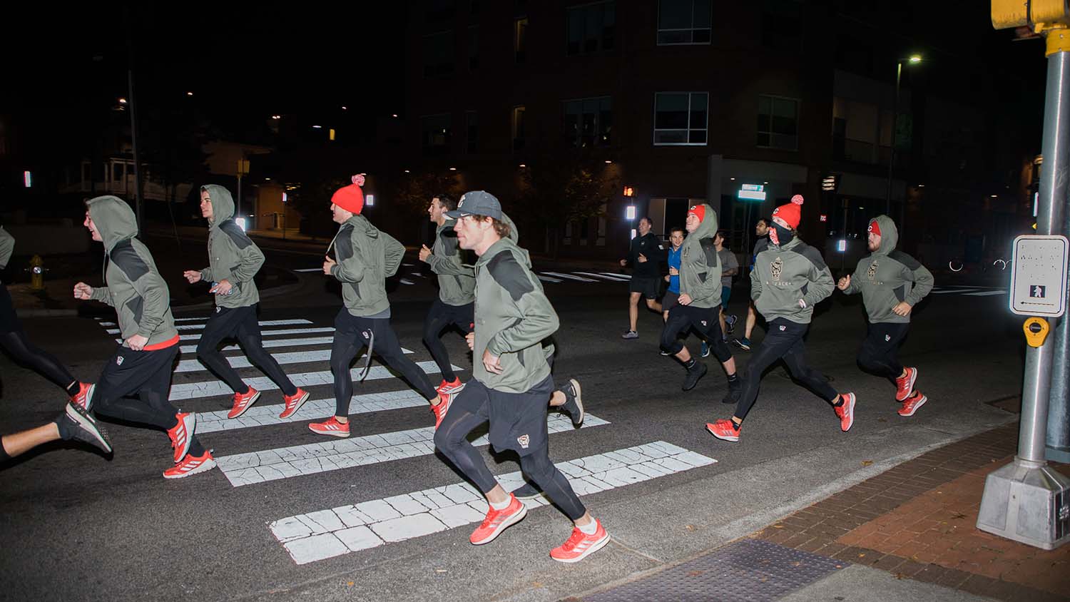 A group of NC State students in matching clothes running at nighttime. 