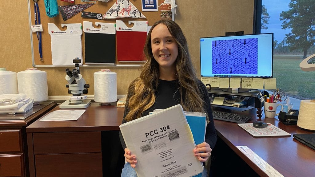 Hannah Rich at her office desk holding notebooks from her TECS classes