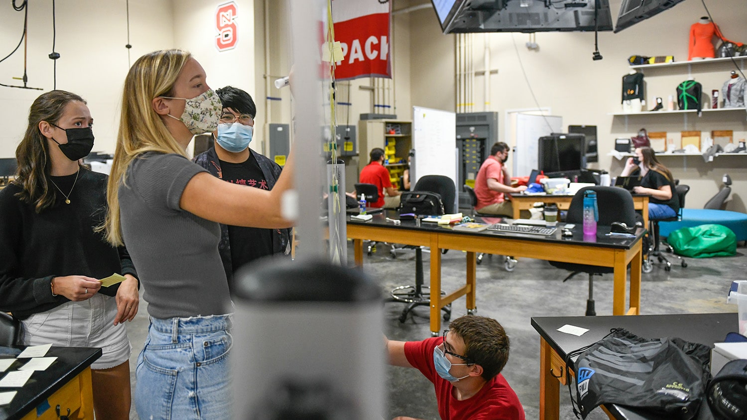 Students work in a textile lab, writing on whiteboards and working in small groups at tables