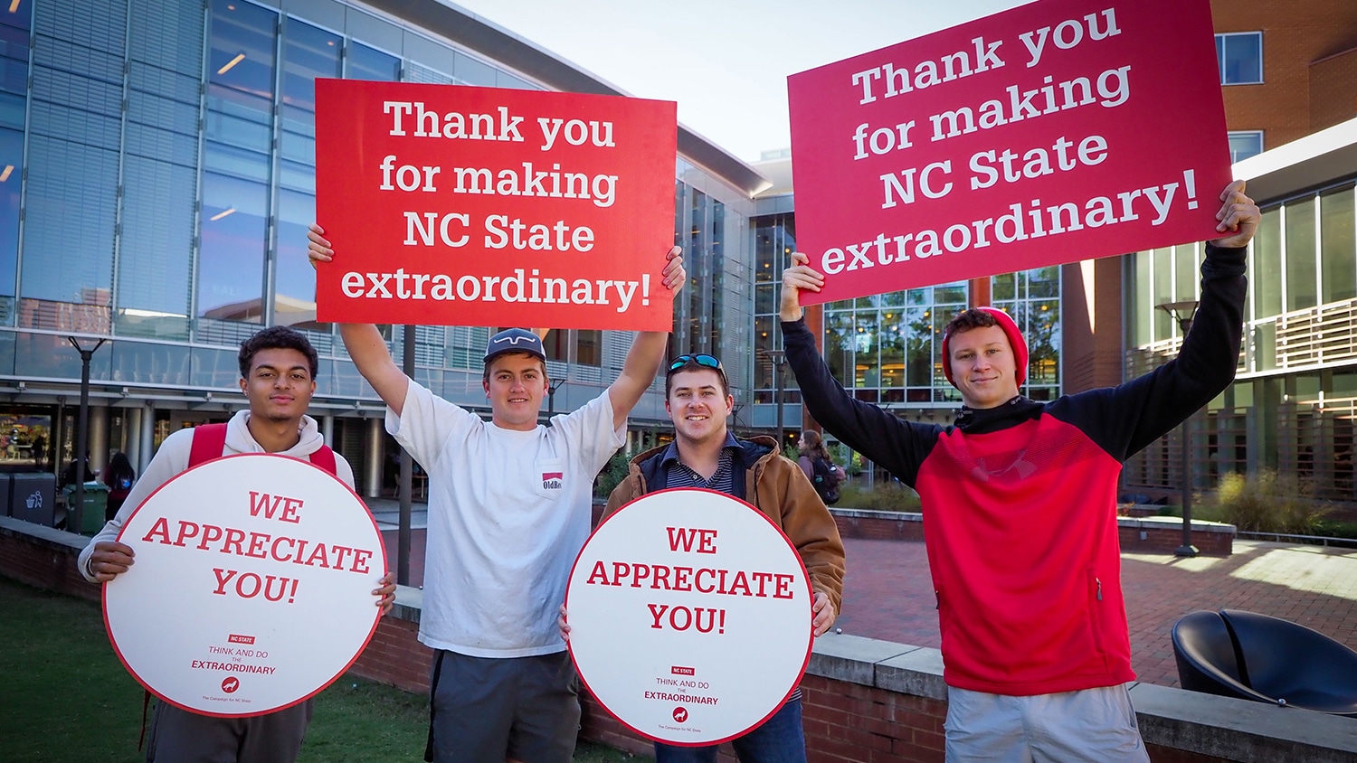 Four students holding up signs thanking NC State donors. 