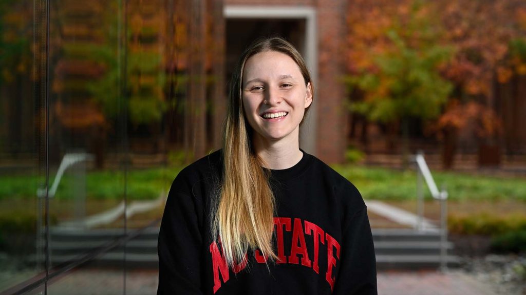 Georgia Burgess standing outside of Fitts-Woolard Hall wearing an NC State sweatshirt.