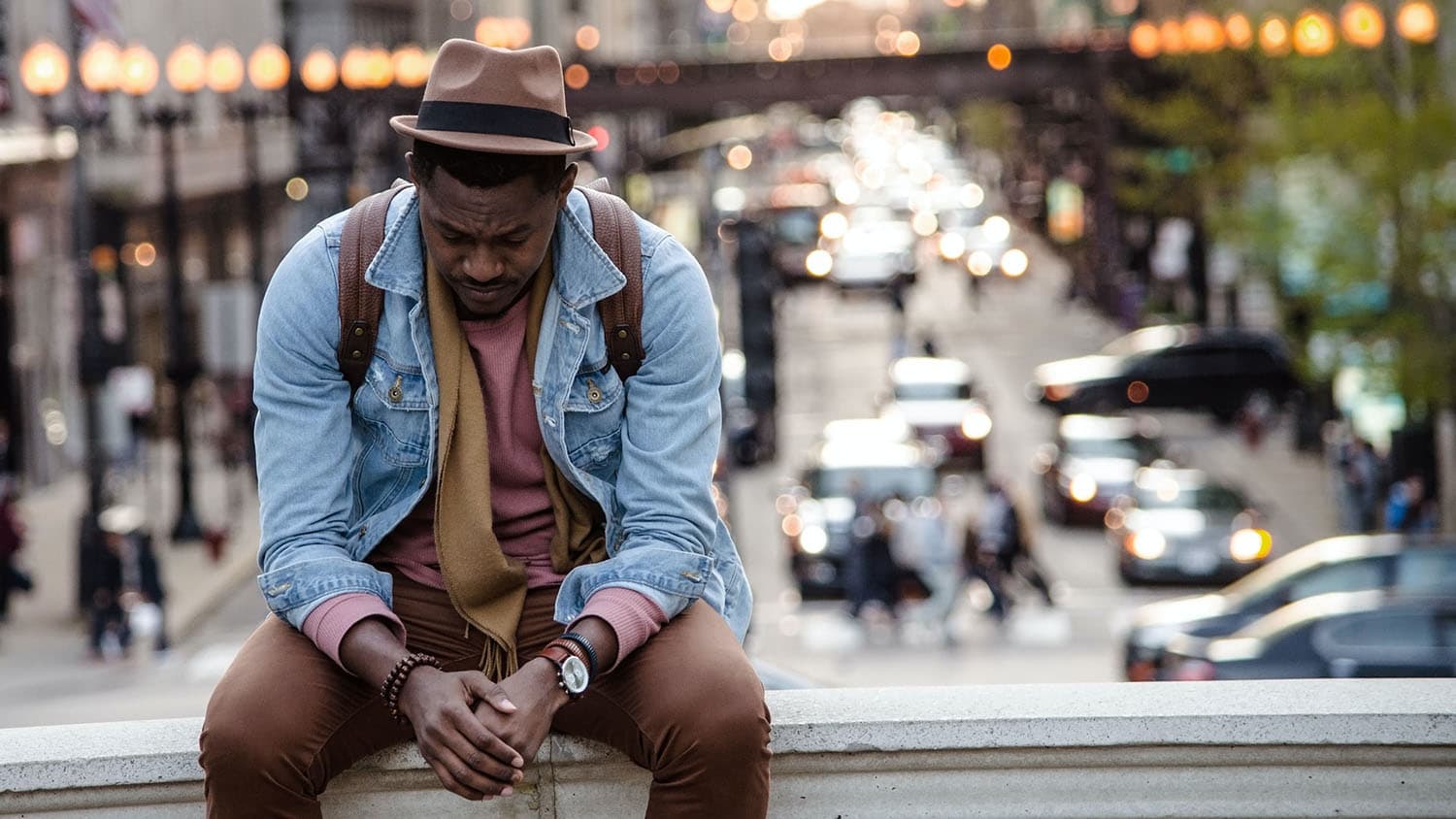 Black man sitting on a city bench looking sad