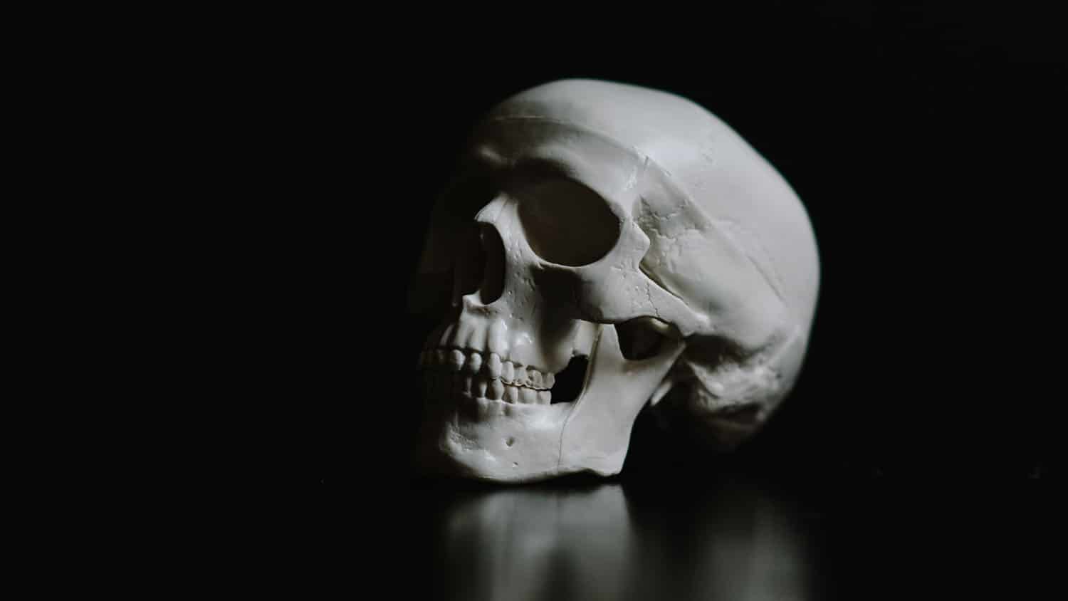 a human skull rests on a glossy black surface in front of a black background
