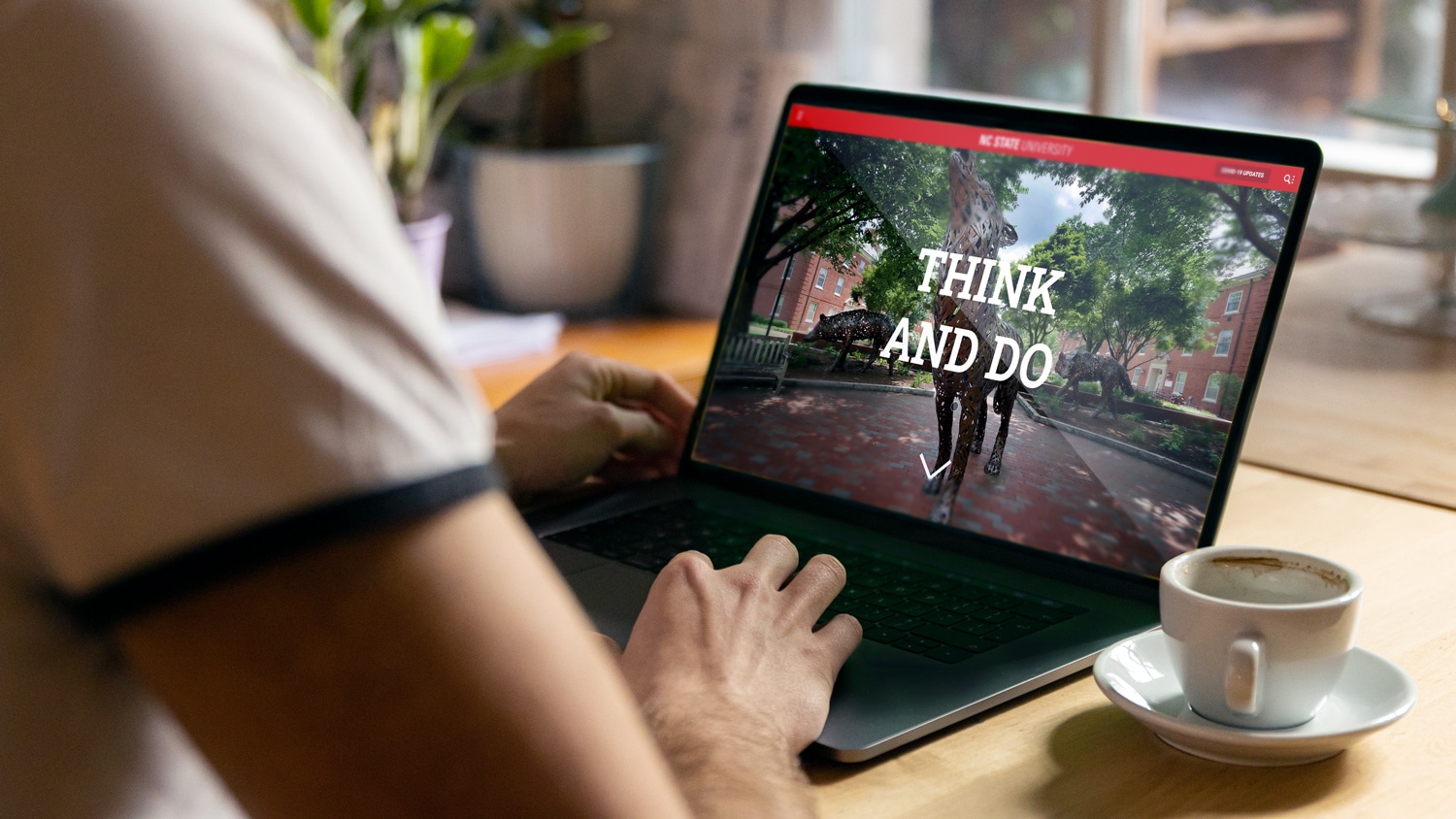 The new NC State website displayed on a laptop next to a cup of coffee.