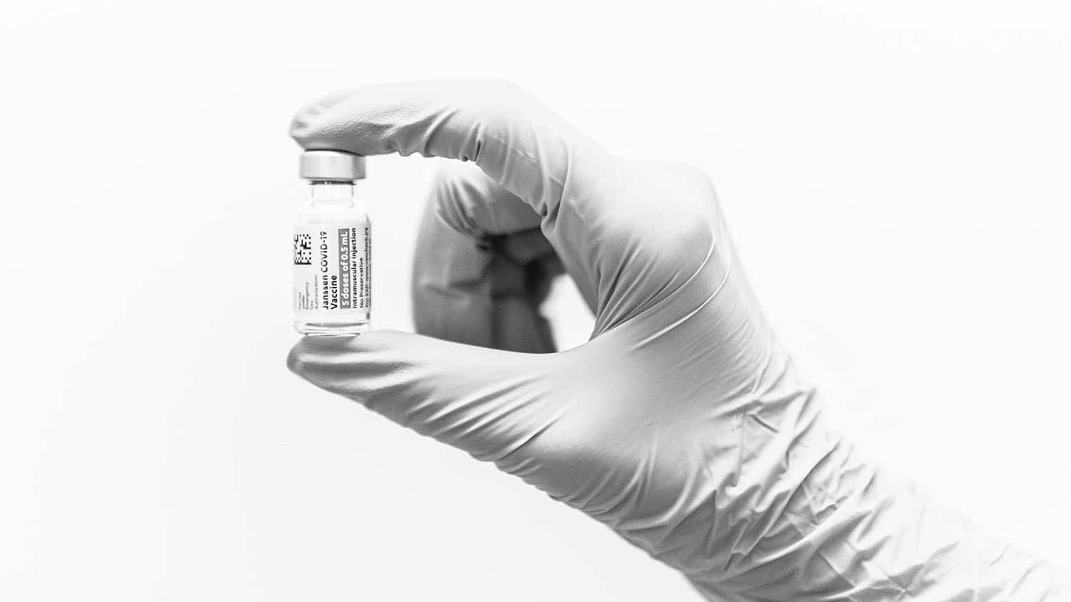 hand wearing a nitrile glove is holding a vial of vaccine