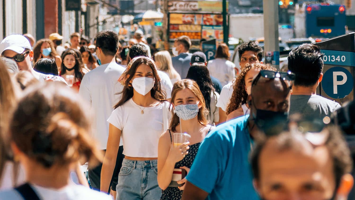a crowd of people walk down the street wearing masks