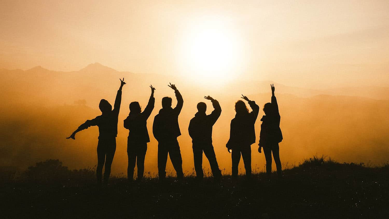 group of people silhouetted against a sunrise