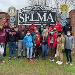A group of students pose for a photo near the welcome sign for Selma.