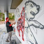 An artist spray-paints a mural outside of Talley.