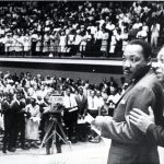 Martin Luther King Jr. stands in Reynolds Coliseum in a black-and-white photo.