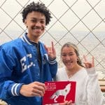 Two students hold up wolf hands and pose with a Day of Giving frame in Paris.