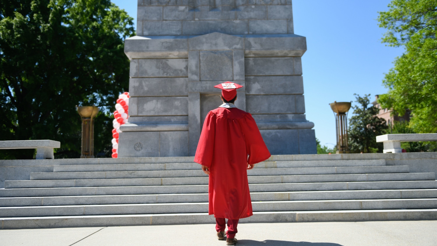 Graduating student dressed in red regalia faces NC State Belltower