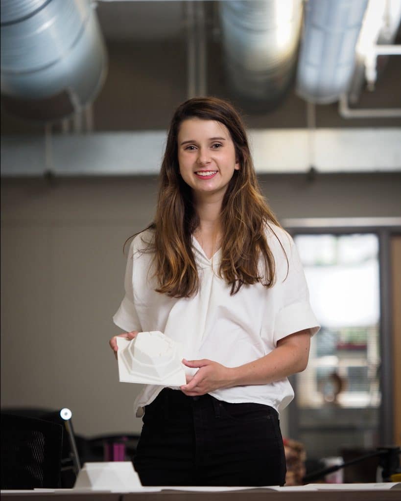 Madelyn Lammert stands in a room holding a white take-out container. 