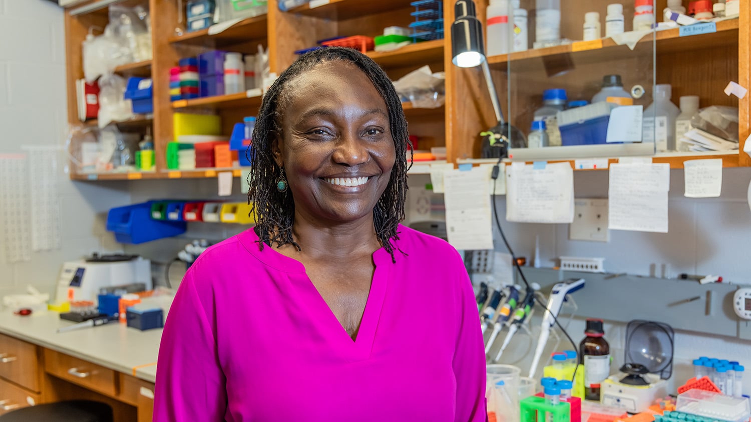 Cathrine Hoyo stands in her lab in front of a shelf filled with lab equipment.