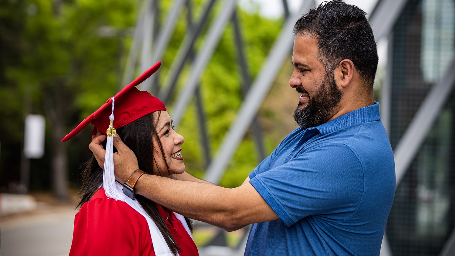 Anna Jump, wearing her red graduation cap and gown, stands with her husband outside of Talley Student Union.