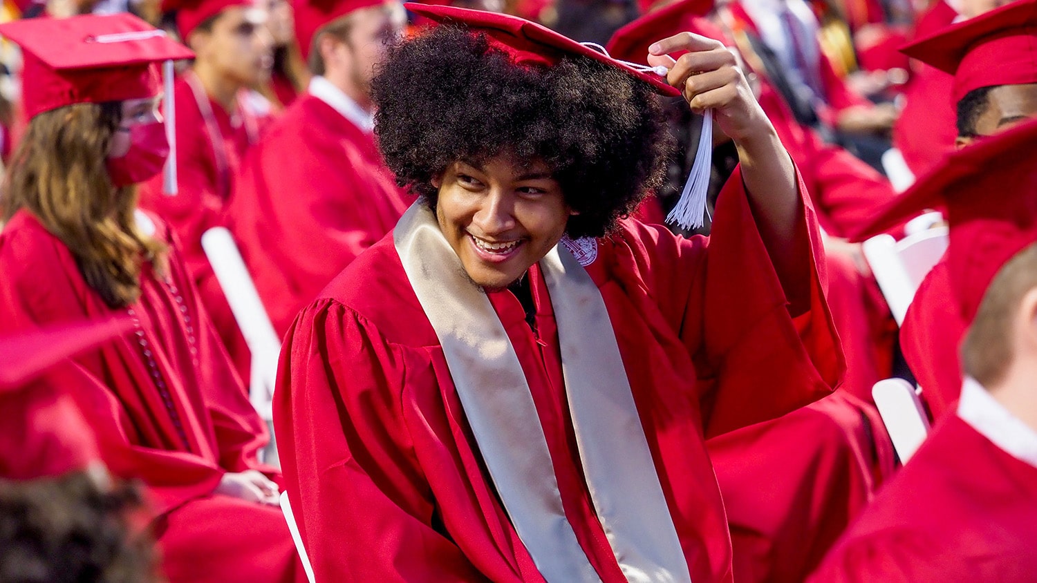 A student turns his tassel among a sea of red-clad graduates during a commencement ceremony