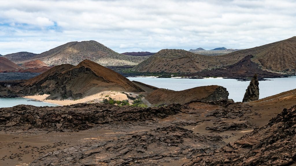 A photo of the landscape on the Galapagos Islands. Hills are made up of volcanic rock and are interspersed with small bodies of water.