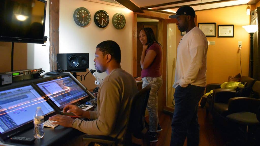Ayo Agunbiade and TreAlise stand behind audio engineer Michael Reeves as he works the mixing board.
