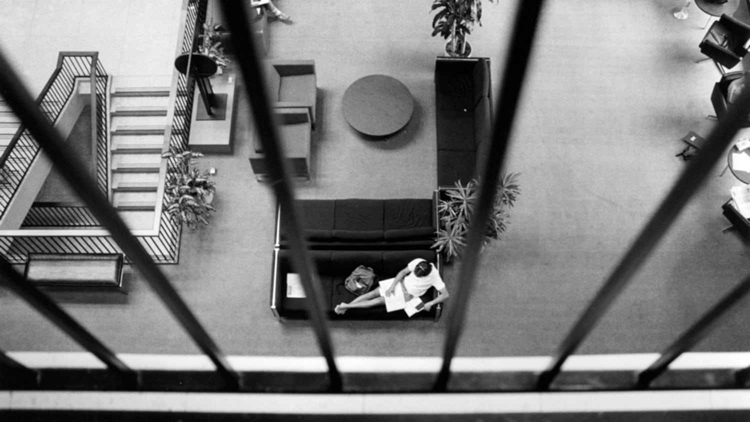 A black and white archival photo shows an overhead view of a student reading books on a couch in the original University Student Center.