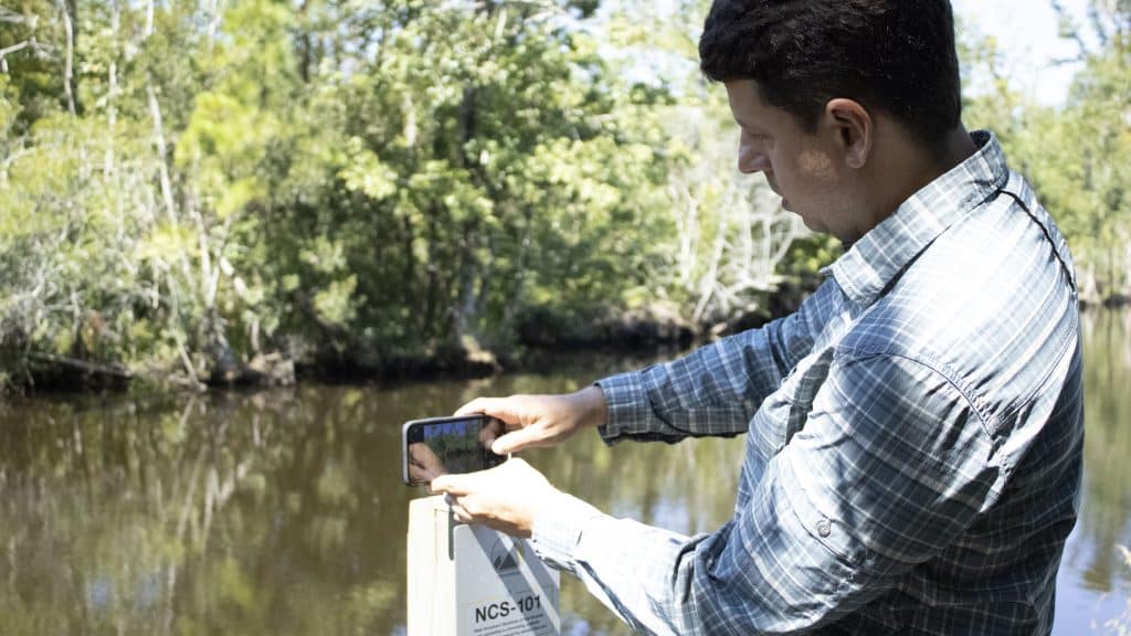 An NC State researcher demonstrates using a citizen science station to take a photo of a forest.