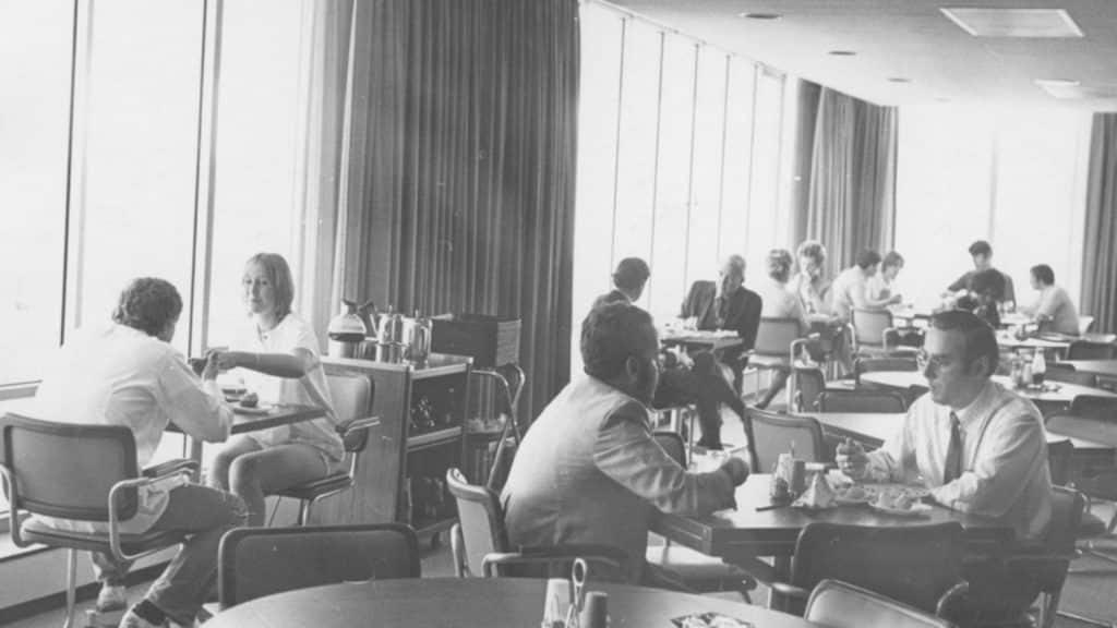 In a black-and-white archival photo, people sit sharing meals throughout the Walnut Room, a cafeteria in the University Student Center.