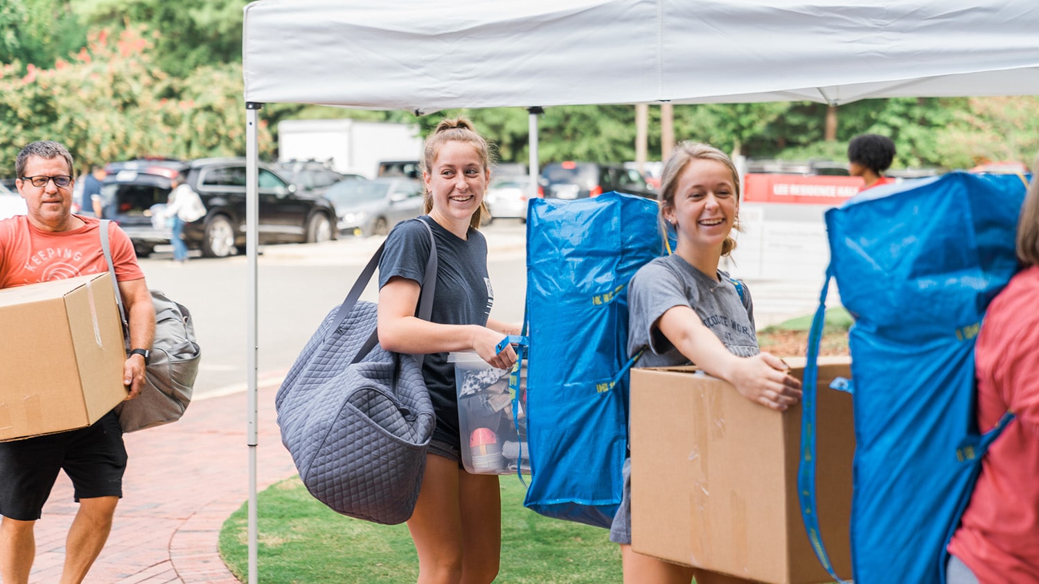 Two students carry boxes toward their residence halls on a sweltering move-in day.