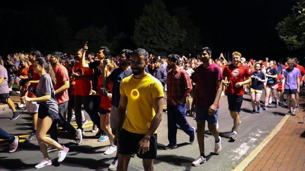A crowd of students walk and run down a road on campus during Moonlight Howl and Run.