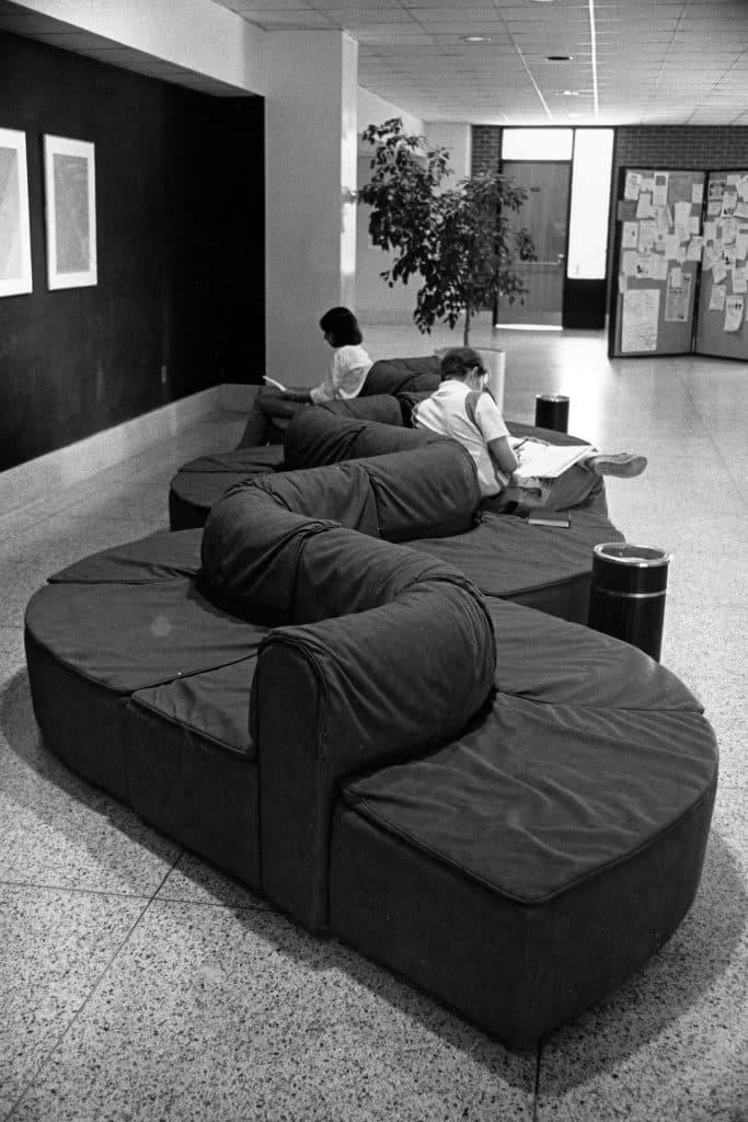 In a black-and-white archival photo, students sit on a curving couch in the student union.