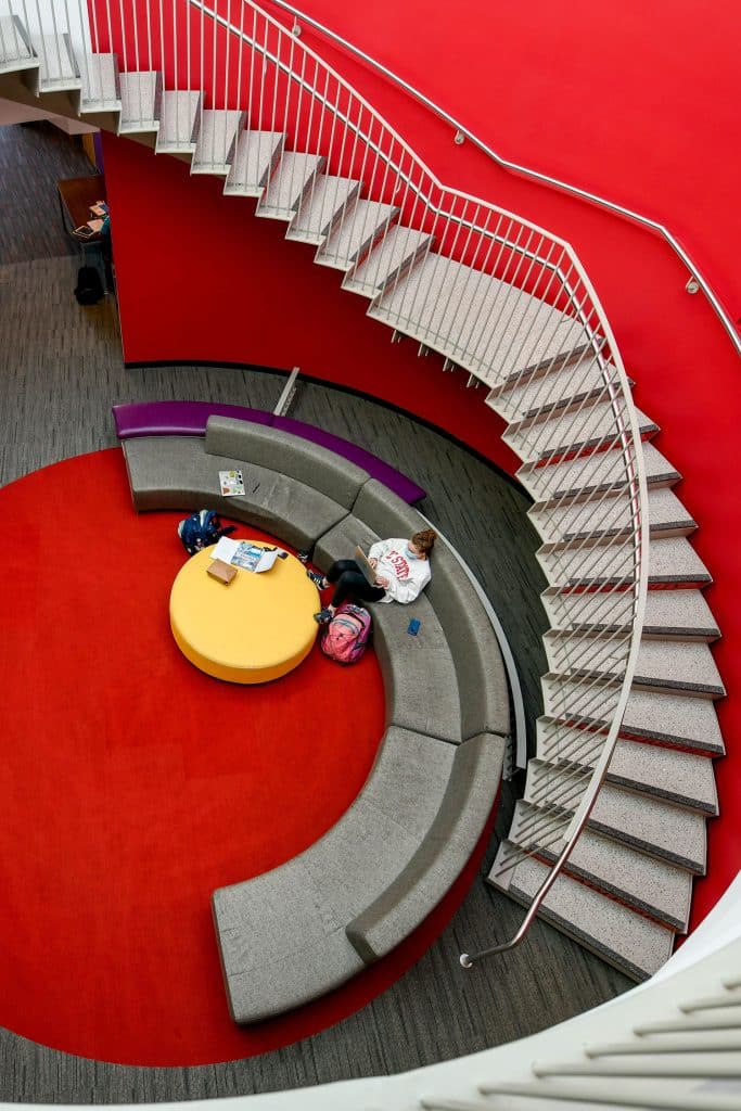 Shot from above, a student sits on a curved couch in a red room in the renovated Talley Student Union.